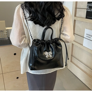 Détail du sac seau noir à cordon avec un grand nœud argenté et une bandoulière en chaîne