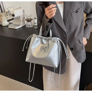Sac seau argenté avec nœud en strass, porté avec un blazer gris et une jupe beige chic