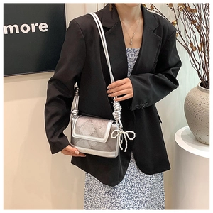 Detail of silver crossbody bag with rhombic texture and pearl bow charm on a model