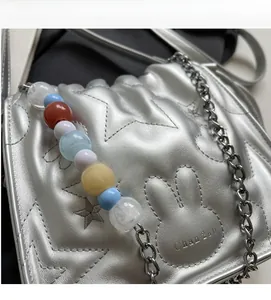 Détail d'un sac seau argenté métallisé avec surpiqûres étoiles et pendentif perles
