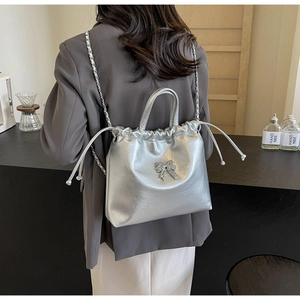 Vue arrière d'un mannequin portant un sac seau argenté avec nœud et bandoulière chaîne