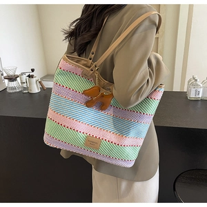 Dettaglio della borsa tote in paglia a righe multicolore con tracolla e ciondolo