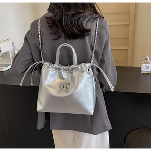 Détail du sac seau métallisé argenté avec décoration de nœud et bretelles en chaîne