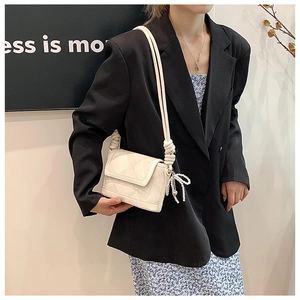 Close-up of cream bucket bag with knotted strap and pearl bow charm on a model