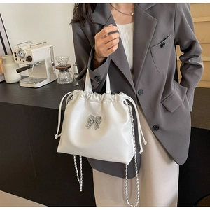 Détail d'un sac seau blanc à cordon avec un nœud argenté orné de diamants et chaîne