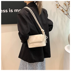 Detail of beige quilted shoulder bag with pearl bow charm and slender strap on model