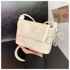 Close-up of beige crossbody bucket bag with diagonal texture and pearl bow charm