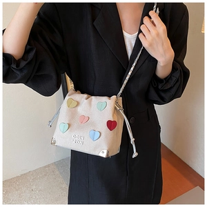 Detail of off-white bucket bag with colorful heart patches and silver chain strap