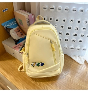 Detail shot of a light yellow nylon backpack showing front zip pocket and RKDBAG embroidery