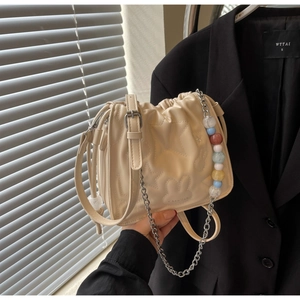 Détail d'un sac seau beige avec motifs étoiles en relief et chaîne de perles colorées