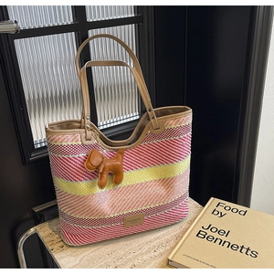 Dettaglio della borsa tote in paglia a righe colorate con manici in pelle e ciondolo