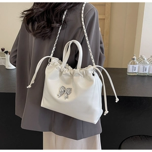 Détail du sac seau blanc avec nœud argenté et bandoulière en chaîne porté par un mannequin