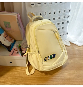 Detail view of a yellow nylon backpack with embroidery on a desk with books