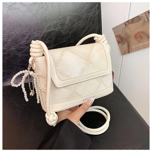 Detail of beige quilted crossbody bag featuring pearl bow and knotted rope strap