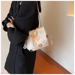 Detail of cream bucket bag with colorful heart patches and silver chain strap