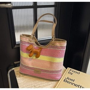 Dettaglio della borsa tote in paglia intrecciata con manici in pelle e ciondolo cane