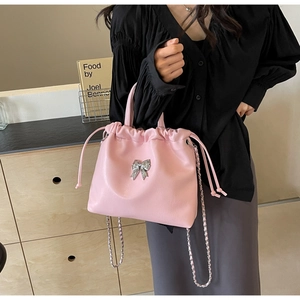 Détail du sac seau rose avec un nœud argenté et une bandoulière en chaîne élégante
