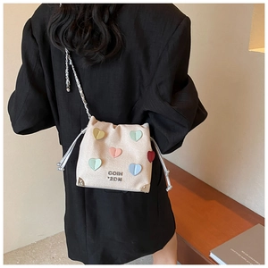 Detail of cream drawstring bucket bag featuring colorful heart patches and silver chain strap