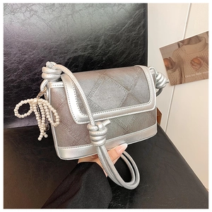 Detail of silver metallic bucket bag with textured surface and pearl bow pendant