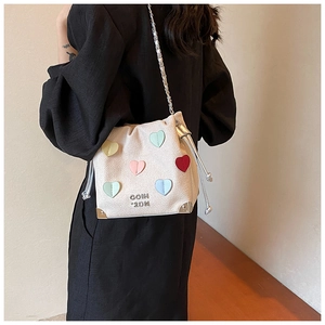 Close-up of cream drawstring bucket bag with colorful heart patches and chain strap