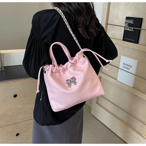 Détail du sac seau rose avec boucle nœud argentée et bandoulière chaîne élégante à l'épaule