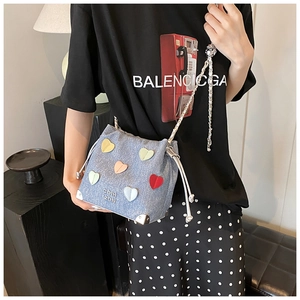 Detail of blue denim bucket bag with colorful 3D heart patches and silver chain strap