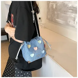 Detail of blue denim bucket bag with colorful heart patches and silver chain strap
