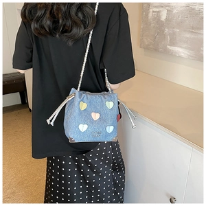 Detail of light blue denim bucket bag with colorful heart patches and chain strap