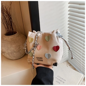 Detail view of beige bucket bag with colorful heart patches and silver chain strap