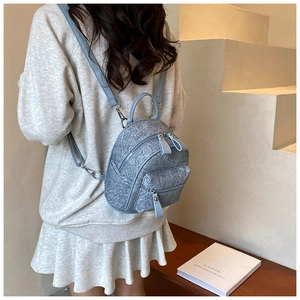 Detail showing the crackle texture and silver zippers on a light blue mini backpack