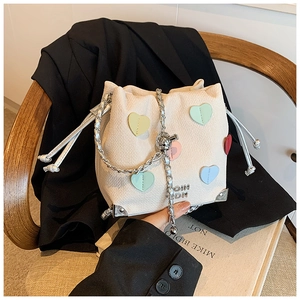 Close-up of cream bucket bag featuring colorful heart patches and silver chain strap