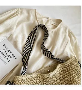 Detail of hand-woven straw tote with striped handles and magnetic closure on shirt