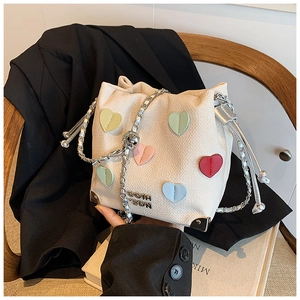 Detail of cream bucket bag with heart patches, chain strap, and metallic brand logo