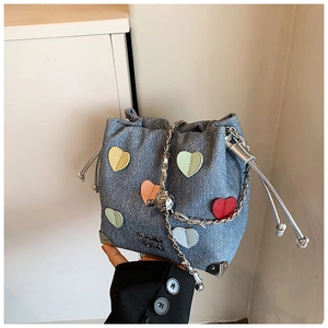Detail of blue denim bucket bag featuring colorful heart patches and silver chain strap