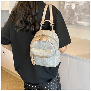 Rear view of a light blue washed denim mini backpack with beige leather straps for women
