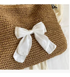 Detailed close-up of woven straw tote bag featuring a large white decorative silk bow