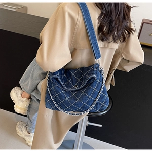 Dettaglio borsa a tracolla in denim blu con cuciture a rombi e catena in metallo argento