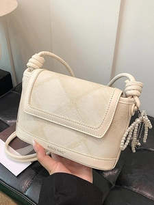 Chic cream bucket bag with geometric texture, knotted strap, and pearl tassel detail