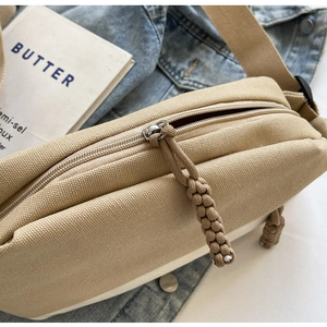 Detail der Canvas-Brusttasche mit Reißverschluss und dekorativem Webknoten-Abzieher