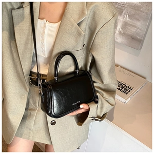 Petit sac noir brillant avec bandoulière argentée porté avec une tenue de bureau