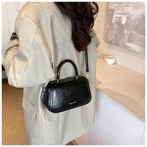 Détail d'un sac bandoulière en cuir noir avec poignée porté sur un costume beige