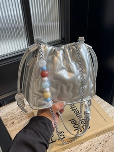 Sac bandoulière argenté avec matelassage étoile et perles colorées tenu à la main