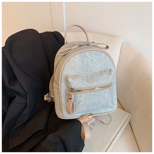 Detail of mini backpack in light blue denim and pink PU leather on a white sofa