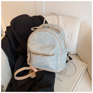 Detail of light blue denim mini backpack with beige leather straps and silver metal zippers