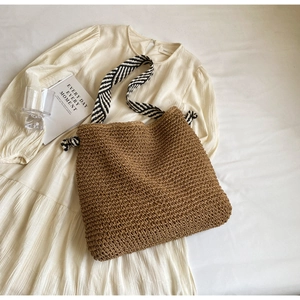Detail of hand-woven straw tote bag with black and white strap and knot accent