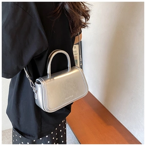 Détail d'un sac bandoulière argenté métallisé avec poignée en arc et sangle sur mannequin