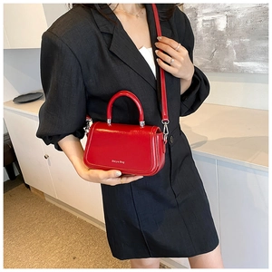 Detailed side view of a glossy red fashion handbag with silver metal hooks and long strap