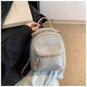 Detail of gray denim mini backpack with light brown leather trim and zipper pocket