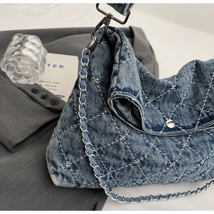 Dettaglio borsa di jeans trapuntata azzurra con catena d'argento su blazer grigio
