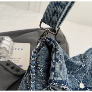 Dettaglio della borsa in denim blu con cuciture trapuntate e attacco della catena argento